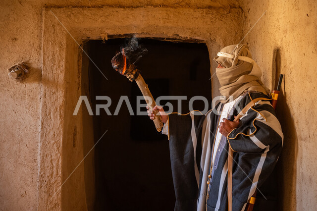 القتال والحرب بالبنادق للحماية وتأسيس الدولة السعودية الأولى 1727م، رجل عربي خليجي سعودي يرتدي الزي الشعبي يحمل البندقية وشعلة النار يقف في بيت طيني، الحراسة والمراقبة للدفاع عن الوطن، الحفاظ على تاريخ وتراث المملكة، يوم بدينا 22 فبراير