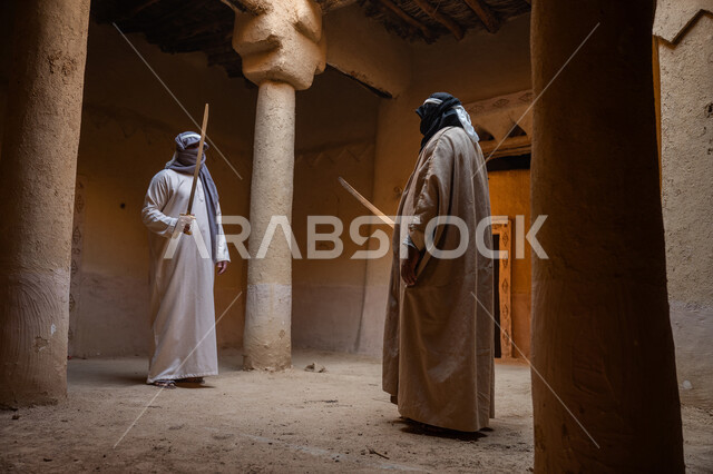 أدوات الحرب القديمة، المبارزة بالسيف للحماية وتأسيس الدولة السعودية الأولى 1727م، رجلان عربيان خليجيان سعوديان يرتديان الزي الشعبي يتبارزان بالسيوف في بيت طيني، مفهوم الحرب والدفاع عن الوطن، الحفاظ على تاريخ وتراث المملكة، يوم بدينا 22 فبراير