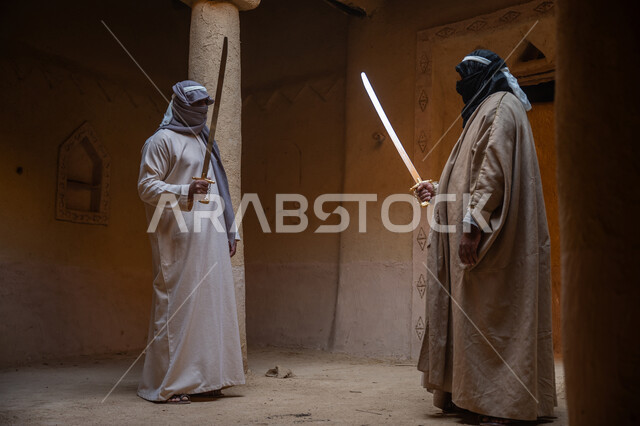 The concept of war and defending the homeland, preserving the history and heritage of the Kingdom, ancient war tools, sword fighting for protection and the establishment of the first Saudi state 1727 AD, two Saudi Gulf Arab men wearing traditional costumes dueling with swords in a mud house, the day we started, February 22