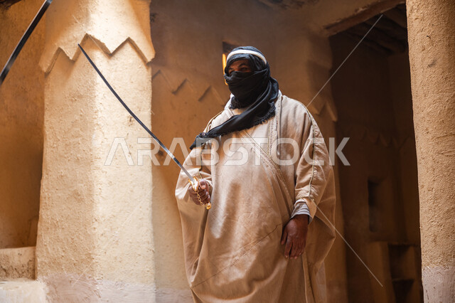 المبارزة بالسيف للحماية وتأسيس الدولة السعودية الأولى 1727م، أدوات الحرب القديمة، رجل عربي خليجي سعودي يرتدي الزي الشعبي يتبارز بالسيوف مع شخص آخر في بيت طيني، مفهوم الحرب والدفاع عن الوطن، الحفاظ على تاريخ وتراث المملكة، يوم بدينا 22 فبراير