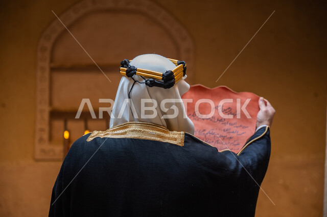 الخطابات والمراسلات التراثية لتأسيس الدولة السعودية الأولى 1727م، الحفاظ على آثار ومخطوطات المملكة، صورة مقربة من الخلف لرجل عربي خليجي سعودي يرتدي الغترة والعقال الذهبي والبشت يقوم بقراءة مخطوطة جلد تاريخية، ارتداء الزي الشعبي في المناسبة الوطنية، يوم بدينا 22 فبراير