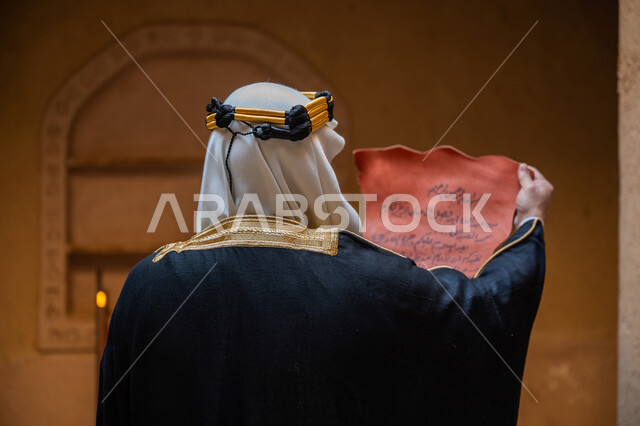 الخطابات والمراسلات التراثية لتأسيس الدولة السعودية الأولى 1727م، الحفاظ على آثار ومخطوطات المملكة، صورة مقربة من الخلف لرجل عربي خليجي سعودي يرتدي الغترة والعقال الذهبي والبشت يقوم بقراءة مخطوطة جلد تاريخية، ارتداء الزي الشعبي في المناسبة الوطنية، يوم بدينا 22 فبراير
