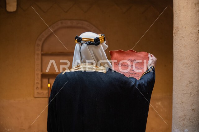 الحفاظ على آثار ومخطوطات المملكة، ارتداء الزي الشعبي في المناسبة الوطنية، الخطابات والمراسلات التراثية لتأسيس الدولة السعودية الأولى 1727م، صورة مقربة من الخلف لرجل عربي خليجي سعودي يرتدي الغترة والعقال الذهبي والبشت يقوم بقراءة مخطوطة جلد تاريخية، يوم بدينا 22 فبراير
