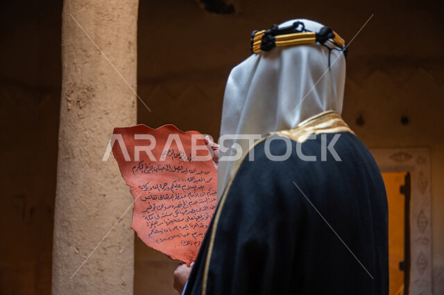 الخطابات والمراسلات التراثية لتأسيس الدولة السعودية الأولى 1727م، الحفاظ على آثار ومخطوطات المملكة، صورة مقربة من الخلف لرجل عربي خليجي سعودي يرتدي الغترة والعقال الذهبي والبشت يقوم بقراءة مخطوطة جلد تاريخية، ارتداء الزي الشعبي في المناسبة الوطنية، يوم بدينا 22 فبراير