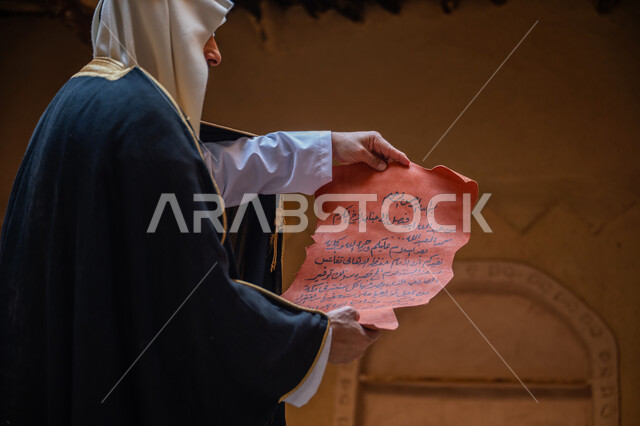 يوم بدينا 22 فبراير، صورة مقربة من الجانب لرجل عربي خليجي سعودي يرتدي الغترة والبشت يقوم بقراءة مخطوطة جلد تاريخية، ارتداء الزي الشعبي في المناسبة الوطنية، الحفاظ على آثار ومخطوطات المملكة، الخطابات والمراسلات التراثية لتأسيس الدولة السعودية الأولى 1727م