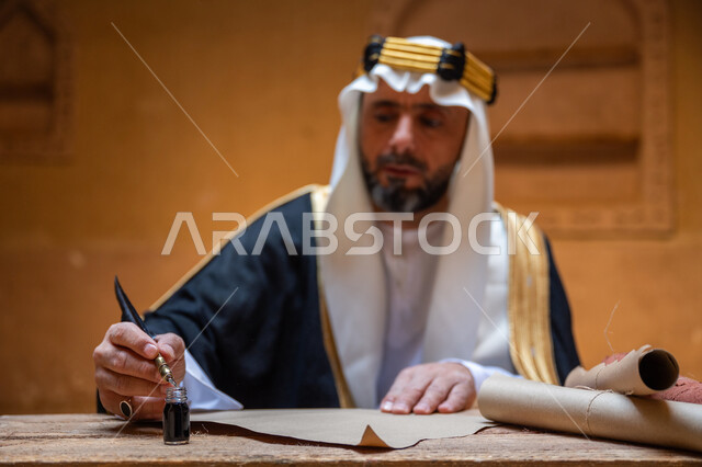 الخطابات والمراسلات التراثية لتأسيس الدولة السعودية الأولى 1727م، الفخر بأصالة المملكة، ارتداء الزي الشعبي في المناسبة الوطنية، صورة مقربة لرجل عربي خليجي سعودي يرتدي الغترة والعقال الذهبي والبشت يمسك بيده الريشة يقوم بالكتابة على مخطوطة جلد تاريخية، يوم بدينا 22 فبراير