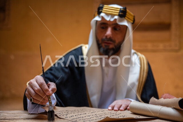 الخطابات والمراسلات التراثية لتأسيس الدولة السعودية الأولى 1727م، الفخر بأصالة المملكة، ارتداء الزي الشعبي في المناسبة الوطنية، صورة مقربة لرجل عربي خليجي سعودي يرتدي الغترة والعقال الذهبي والبشت يمسك بيده الريشة يقوم بالكتابة على مخطوطة جلد تاريخية، يوم بدينا 22 فبراير