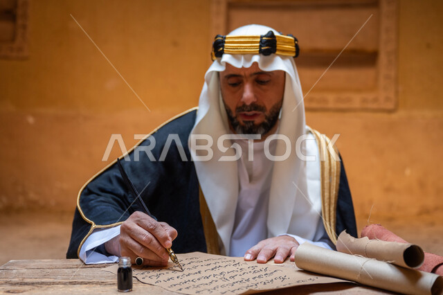 الخطابات والمراسلات التراثية لتأسيس الدولة السعودية الأولى 1727م، الفخر بأصالة المملكة، ارتداء الزي الشعبي في المناسبة الوطنية، صورة مقربة لرجل عربي خليجي سعودي يرتدي الغترة والعقال الذهبي والبشت يمسك بيده الريشة يقوم بالكتابة على مخطوطة جلد تاريخية، يوم بدينا 22 فبراير