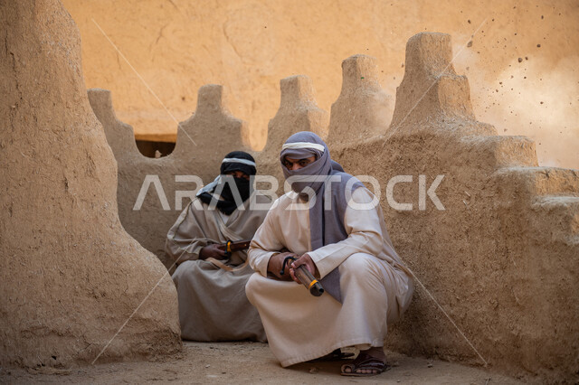 مفهوم الحراسة والمراقبة، يوم بدينا 22 فبراير, جنديان عربيان خليجيان سعوديان ملثمان يرتديان الزي الشعبي في المناسبة الوطنية يحملان البندقية يحتميان خلف جدار طيني، القتال والحرب لحماية البلاد, حمل السلاح للدفاع عن الوطن, إحياء ذكرى يوم تأسيس الدولة السعودية 1727 م