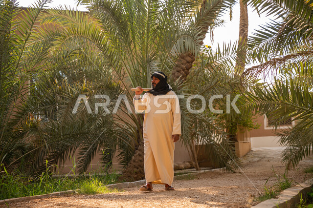 يوم بدينا 22 فبراير, إحياء ذكرى تأسيس الدولة السعودية الأولى 1727 م, مهنة وحرفة شعبية تراثية, تشجير وزراعة الأراضي السعودية, فلاح عربي خليجي سعودي يرتدي الزي التقليدي يمسك بيده أداة خاصة بحراثة الأرض, توارث مهنة الفلاحة, مزرعة أشجار النخيل في المملكة