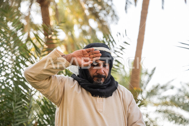 إحياء ذكرى تأسيس الدولة السعودية الأولى 1727 م, مزرعة أشجار النخيل في المملكة, يوم بدينا 22 فبراير, صورة مقربة لفلاح عربي خليجي سعودي يرتدي الزي التقليدي يقوم بمسح جبهته بيده, توارث مهنة الفلاحة, مهنة وحرفة شعبية تراثية, تشجير وزراعة الأراضي السعودية