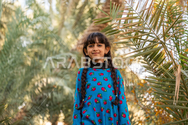 The concept of softness and innocence, commemorating the Saudi Founding Day 1727 AD, the day we started February 22, a Saudi Gulf Arab girl wearing the Founding Day costume stands in a palm farm and looks at the camera with gestures of happiness and pleasure, elegance and interest in the external appearance, a natural reserve for planting palm trees