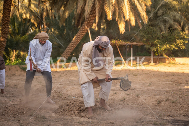 مزرعة أشجار النخيل في المملكة, حرفة شعبية تراثية, زراعة وتشجير الأراضي السعودية, إحياء ذكرى تأسيس الدولة السعودية الأولى 1727 م, يوم بدينا 22 فبراير, فلاحان عربيان خليجيان سعوديان يرتديان الزي التقليدي يقومان بحراثة الأرض, توارث مهنة الفلاحة