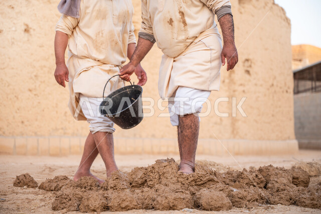 إحياء ذكرى يوم التأسيس1727 م, بناء الدولة السعودية الأولى، يوم بدينا 22 فبراير, عاملان عربيان يقومان بعجن الطين بأقدامهم, الفخر والاعتزاز بالتراث السعودي العريق, تشييد وبناء البيوت الطينية التراثية التاريخية