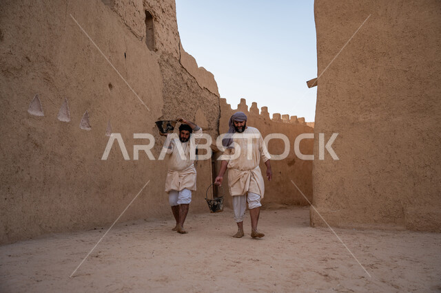 تشييد وبناء البيوت الطينية التراثية التاريخية, إحياء ذكرى يوم التأسيس1727 م, بناء الدولة السعودية الأولى, عاملان عربيان يقومان بنقل الطين ومواد البناء, يوم بدينا 22 فبراير, الفخر والاعتزاز بالتراث السعودي العريق