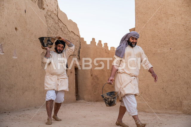Pride and honor in the ancient Saudi heritage, construction and building of historical heritage mud houses, commemorating the founding day 1727 AD, building the first Saudi state, two Arab workers transporting mud and building materials, the day we started, February 22