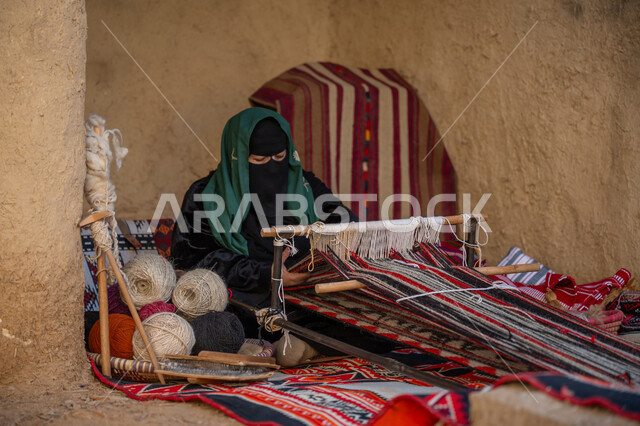 مهنة تقليدية قديمة, يوم بدينا 22 فبراير، ارتداء الزي الشعبي في المناسبة الوطنية, حرفة يدوية تاريخية، امرأة عربية خليجية سعودية ترتدي العباءة والبرقع تجلس في بيت من الطين وتقوم بحياكة وغزل الأنسجة والقماش, منتج محلي وطني، ذكرى تأسيس الدولة السعودية الأولى في 1727م