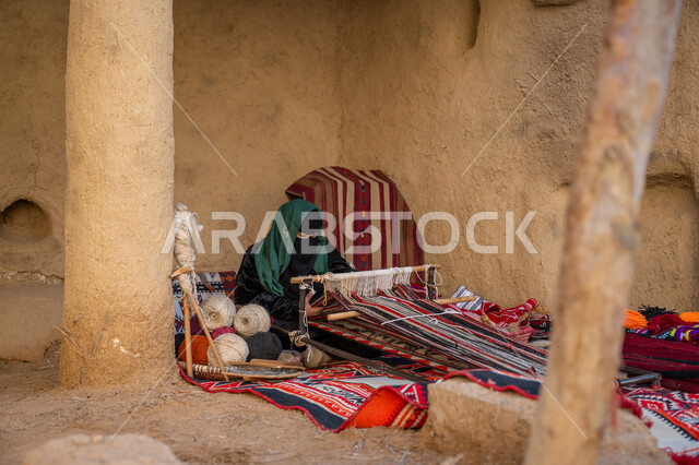 حرفة يدوية تاريخية, مهنة تقليدية قديمة, يوم بدينا 22 فبراير، ارتداء الزي الشعبي في المناسبة الوطنية، امرأة عربية خليجية سعودية ترتدي العباءة والبرقع تجلس في بيت من الطين وتقوم بحياكة وغزل الأنسجة والقماش, منتج محلي وطني، ذكرى تأسيس الدولة السعودية الأولى في 1727م