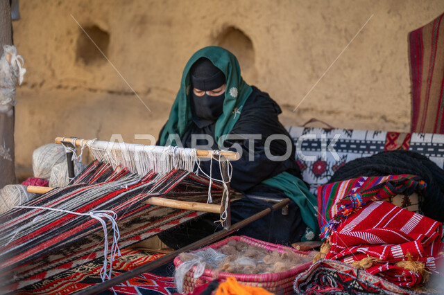مهنة تقليدية قديمة, يوم بدينا 22 فبراير، ارتداء الزي الشعبي في المناسبة الوطنية, حرفة يدوية تاريخية، امرأة عربية خليجية سعودية ترتدي العباءة والبرقع تجلس في بيت من الطين وتقوم بحياكة وغزل الأنسجة والقماش, منتج محلي وطني، ذكرى تأسيس الدولة السعودية الأولى في 1727م
