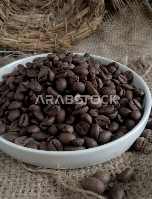 منتج محلي وطني سعودي، صورة مقربة لطبق مليء بحبوب البن المحمصة باللون البني الداكن، جودة المحصول الصناعي الغذائي في المملكة العربية السعودية، اعداد وتحضير القهوة الطازجة