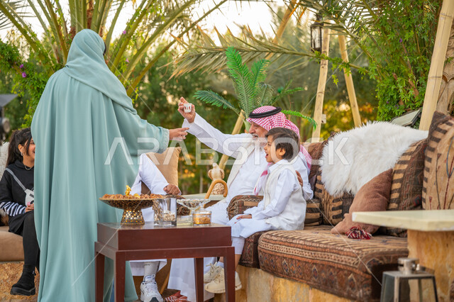 Eid customs in Saudi society, the concept of generosity and hospitality, a Saudi Arabian Gulf woman wearing an abaya serving Arabic coffee to guests, gestures of joy and happiness, a family gathering in the outdoor garden of the house, interest in planting trees and green plants