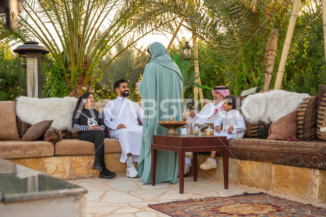 The concept of generosity and hospitality, Eid customs in Saudi society, a Saudi Arabian Gulf woman wearing an abaya serving Arabic coffee to guests, gestures of joy and happiness, a family gathering in the outdoor garden of the house, interest in planting trees and green plants