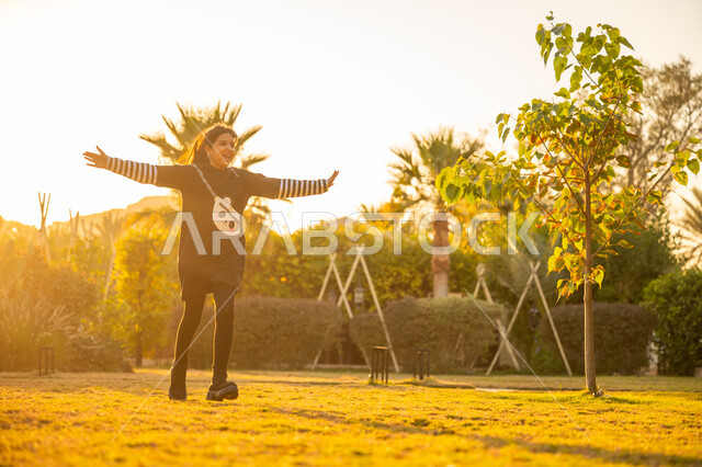 الاستمتاع باللعب والتنزه في الهواء الطلق، الترفيه والتسلية في الحديقة العامة، فتاة عربية خليجية سعودية ترتدي فستان أسود تركض في الحديقة بإيماءات السرور والسعادة، نشاط حركي وفعالية ترفيهية، قضاء وقت ممتع ومسلي في المنتزه