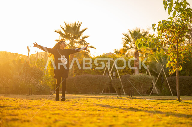 نشاط حركي وفعالية ترفيهية، الاستمتاع باللعب والتنزه في الهواء الطلق، الترفيه والتسلية في الحديقة العامة، فتاة عربية خليجية سعودية ترتدي فستان أسود تركض في الحديقة بإيماءات السرور والسعادة، قضاء وقت ممتع ومسلي في المنتزه