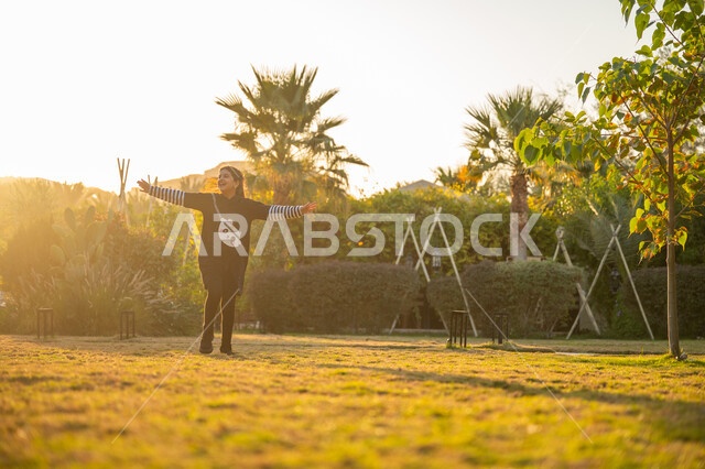 فعالية ترفيهية ونشاط حركي، الاستمتاع باللعب والتنزه في الهواء الطلق، الترفيه والتسلية في الحديقة العامة، فتاة عربية خليجية سعودية ترتدي فستان أسود تركض في الحديقة بإيماءات السرور والسعادة، قضاء وقت ممتع ومسلي في المنتزه