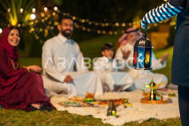 زينة وديكور المناسبات والأعياد الاسلامية، ايماءات السعادة والسرور بالاجتماع العائلي، أجواء عائلية سعيدة في شهر رمضان المبارك، أسرة عربية خليجية سعودية تقضي وقت ممتع في جلسة خارجية في احدى الشاليهات، صورة مقربة ليد فتاة تحمل فانوس معدني مضيء