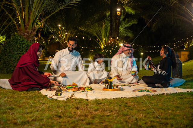 Expressions of happiness and joy at a family gathering, decorations for Islamic occasions and holidays, happy family atmosphere in the holy month of Ramadan, a Saudi Arabian Gulf family spending a pleasant time in an outdoor session in one of the chalets, a girl holding a lit metal lantern in her hand