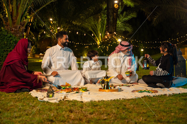 ديكور وزينة المناسبات والأعياد الاسلامية، أجواء عائلية سعيدة في شهر رمضان المبارك، ايماءات السعادة والسرور بالاجتماع العائلي، أسرة عربية خليجية سعودية تقضي وقت ممتع في جلسة خارجية في احدى الشاليهات، فتاة تحمل بيدها فانوس معدني مضيء