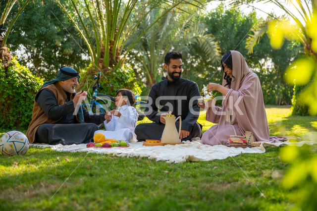 Strengthening and enhancing family ties, exchanging conversations with gestures of pleasure, a Saudi Arabian Gulf family wearing traditional dress sitting in a public park during the day, spending quality time with family, a family amusement park and garden, enjoying a picnic in the open air