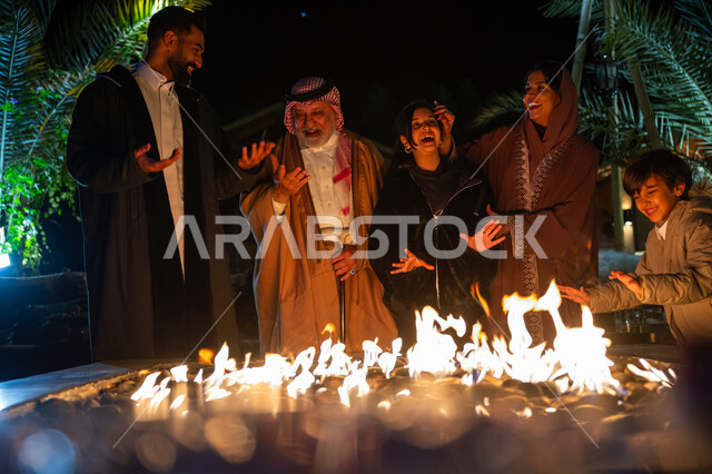 قضاء وقت عائلي ممتع، تبادل الأحاديث والتسامر في كشتة بر في الأجواء الشتوية، التجمع حول الموقد للتدفئة، عائلة عربية خليجية سعودية يستمتعون في إحدى الشاليهات السياحية في المملكة، ايماءات السعادة والسرور والاستمتاع