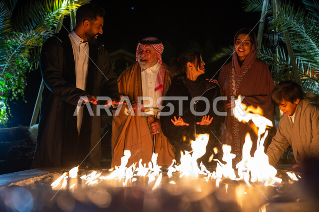 تبادل الأحاديث والتسامر في كشتة بر في الأجواء الشتوية، التجمع حول الموقد للتدفئة، عائلة عربية خليجية سعودية يستمتعون في إحدى الشاليهات السياحية في المملكة، قضاء وقت عائلي ممتع، ايماءات السعادة والسرور والاستمتاع