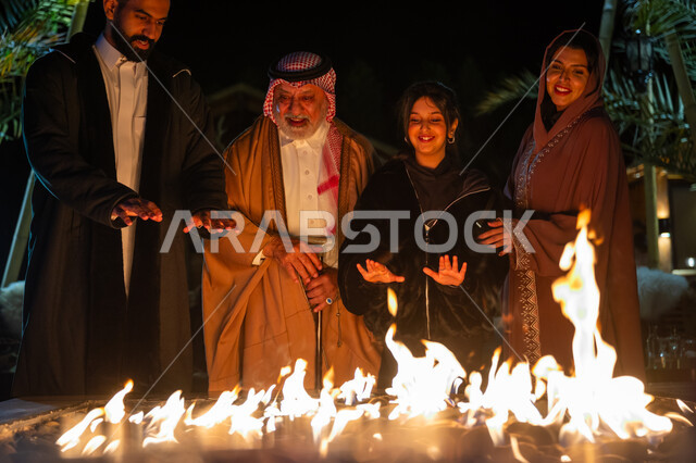 Chatting and exchanging conversations in a desert outing in the winter, gathering around the fireplace to warm up, a Saudi Arabian Gulf family enjoying themselves in one of the tourist chalets in the Kingdom, spending a fun family time, gestures of happiness, pleasure and enjoyment