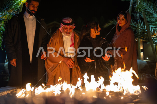 التجمع حول الموقد للتدفئة، التسامر وتبادل الأحاديث في كشتة بر في الأجواء الشتوية، عائلة عربية خليجية سعودية يستمتعون في إحدى الشاليهات السياحية في المملكة، قضاء وقت عائلي ممتع، ايماءات السعادة والسرور والاستمتاع