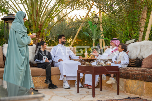 تبادل الأحاديث والأخبار بإيماءات السرور, تقوية وتعزيز الرابط الأسري, الاستمتاع بالمشروب الساخن, عائلة عربية خليجية سعودية يقضون وقت ممتع في الحديقة في النهار, جلسة عائلية بالهواء الطلق, الأجواء الأسرية السعيدة