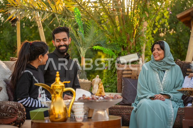 الاستمتاع بالمشروب الساخن, تقوية وتعزيز الرابط الأسري, عائلة عربية خليجية سعودية يقضون وقت ممتع في الحديقة في النهار, جلسة عائلية بالهواء الطلق, الأجواء الأسرية السعيدة, تبادل الأحاديث والأخبار بإيماءات السرور