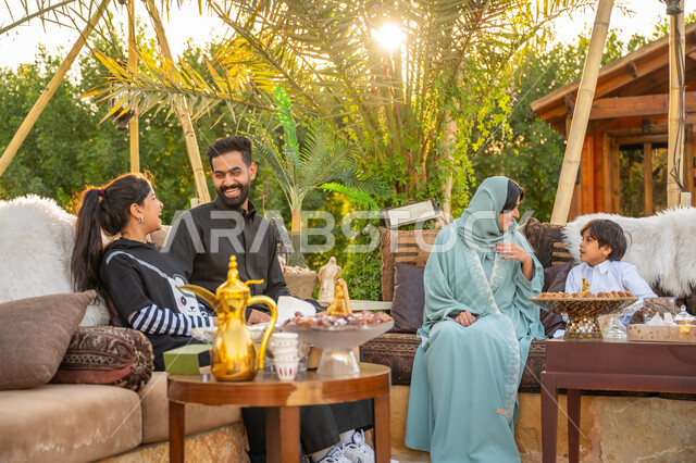 تبادل الأحاديث والأخبار بإيماءات السرور, تقوية وتعزيز الرابط الأسري, الاستمتاع بالمشروب الساخن, عائلة عربية خليجية سعودية يقضون وقت ممتع في الحديقة في النهار, جلسة عائلية بالهواء الطلق, الأجواء الأسرية السعيدة