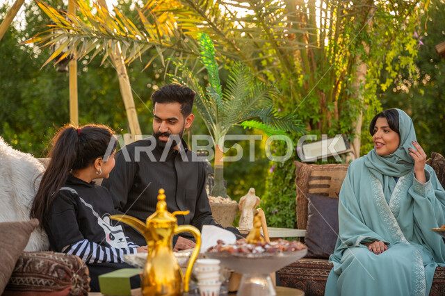 الأجواء الأسرية السعيدة, تبادل الأحاديث والأخبار بإيماءات السرور, تقوية وتعزيز الرابط الأسري, الاستمتاع بالمشروب الساخن, عائلة عربية خليجية سعودية يقضون وقت ممتع في الحديقة في النهار, جلسة عائلية بالهواء الطلق