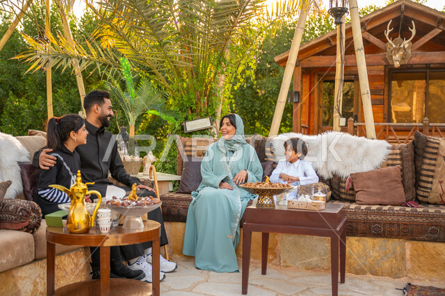 تبادل الأحاديث والأخبار بإيماءات السرور, تقوية وتعزيز الرابط الأسري, الاستمتاع بالمشروب الساخن, عائلة عربية خليجية سعودية يقضون وقت ممتع في الحديقة في النهار, جلسة عائلية بالهواء الطلق, الأجواء الأسرية السعيدة