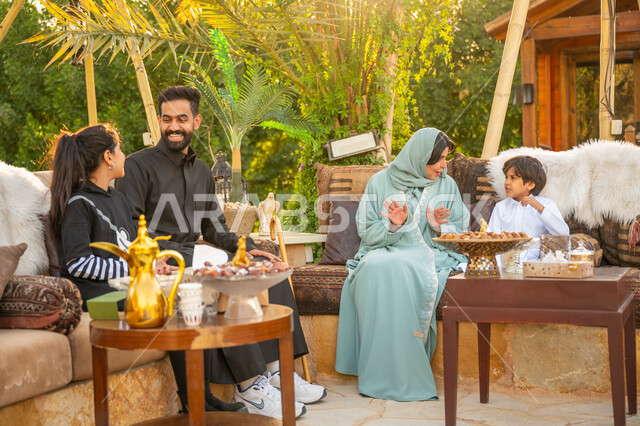 الأجواء الأسرية السعيدة, تبادل الأحاديث والأخبار بإيماءات السرور, تقوية وتعزيز الرابط الأسري, الاستمتاع بالمشروب الساخن, عائلة عربية خليجية سعودية يقضون وقت ممتع في الحديقة في النهار, جلسة عائلية بالهواء الطلق