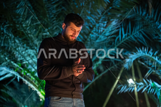 الشعور بالصقيع والبرد الشديد، الأجواء الشتوية الباردة في أماكن التخييم، رجل عربي خليجي سعودي يرتدي الزي الكاجوال ويقوم بحك يديه ببعضهما للشعور بالدفء، قضاء وقت ممتع في الإجازة، جلسة وكشتة بر في منطقة طبيعية بالمملكة العربية السعودية