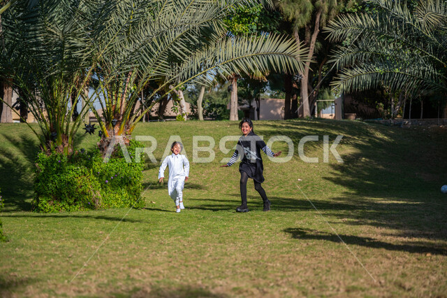 Spending quality time with siblings, playing, having fun and having fun, enjoying outdoor activities, family park and amusement park, Saudi Arabian Gulf girl in casual wear running in a park with her little brother during the day