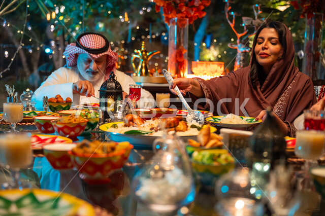 سفرة مليئة بأصناف من المأكولات الشرقية الشهية، أجواء عائلية دينية رمضانية سعيدة، ديكور وزينة المناسبات الإسلامية، تبادل الأحاديث بين أفراد الأسرة، أداء فريضة الصيام في شهر رمضان المبارك، عائلة عربية خليجية سعودية مجتمعة حول مائدة الطعام