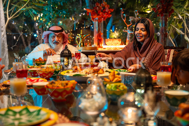 تبادل الأحاديث بين أفراد الأسرة، أداء فريضة الصيام في شهر رمضان المبارك، سفرة مليئة بأصناف من المأكولات الشرقية الشهية، أجواء عائلية دينية رمضانية سعيدة، عائلة عربية خليجية سعودية مجتمعة حول مائدة الطعام، زينة المناسبات الإسلامية
