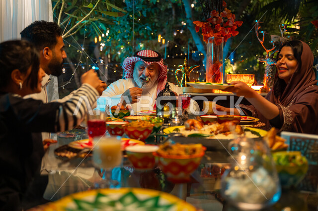 أداء فريضة الصيام في شهر رمضان المبارك، سفرة مليئة بأصناف من المأكولات الشرقية الشهية، أجواء عائلية دينية رمضانية سعيدة، عائلة عربية خليجية سعودية مجتمعة حول مائدة الطعام، تبادل الأحاديث بين أفراد الأسرة، زينة المناسبات الإسلامية