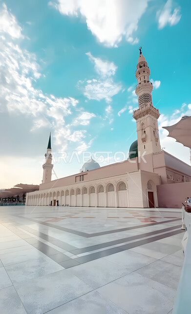 مقصد المسلمين من شتى أنحاء العالم, مكان ديني إسلامي مقدس، القبة الخضراء و المآذن للمسجد النبوي الشريف في المدينة المنورة في النهار، التصميم والديكور الداخلي على الطراز الإسلامي في السعودية, العبادة والتقرب الى الله تعالى, خلفية السماء الزرقاء مع الغيوم
