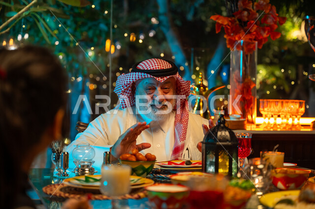 ايماءات السعادة والسرور بلمة الأهل، تناول الافطار الرمضاني عند أذان المغرب, رجل مسن عربي خليجي سعودي يرتدي الثوب التقليدي والشماغ يقضي وقت ممتع مع اسرته على مائدة مليئة بالأطعمة والمشروبات الشهية, جلسة عائلية رمضانية روحانية، زينة وديكور شهر رمضان المبارك
